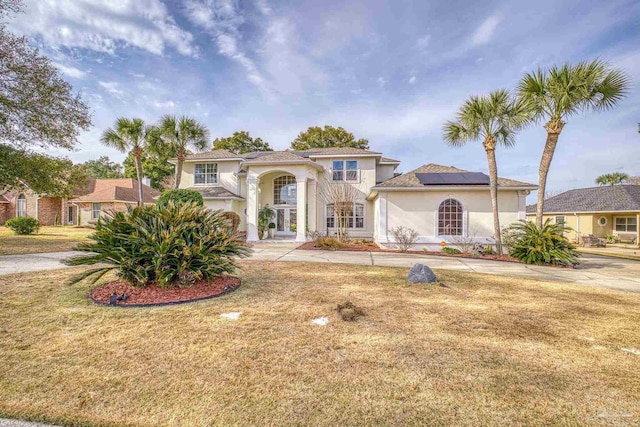 mediterranean / spanish-style house with a front yard, roof mounted solar panels, and stucco siding