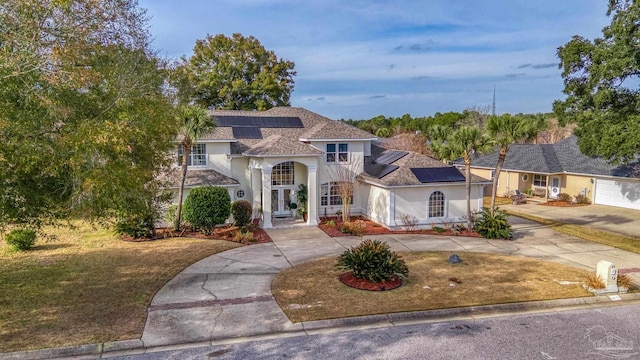 view of front of property featuring a shingled roof, solar panels, driveway, and stucco siding