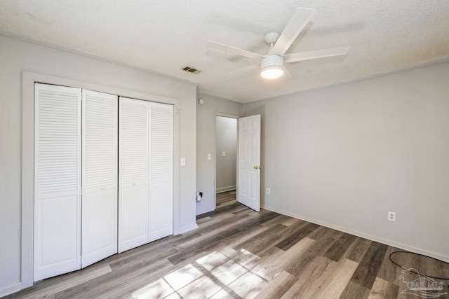 unfurnished bedroom featuring ceiling fan, a closet, wood-type flooring, and a textured ceiling