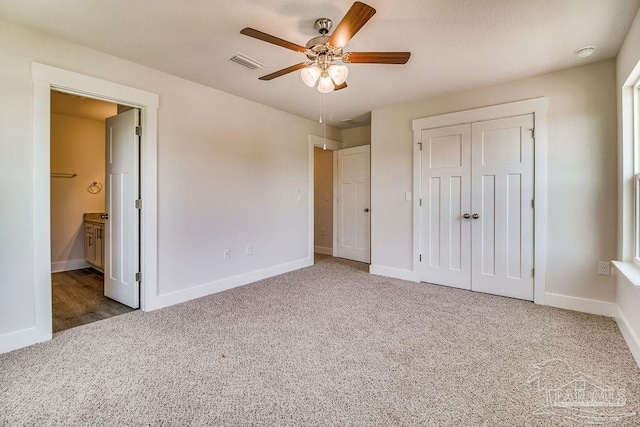 unfurnished bedroom featuring ceiling fan, dark carpet, connected bathroom, and a closet