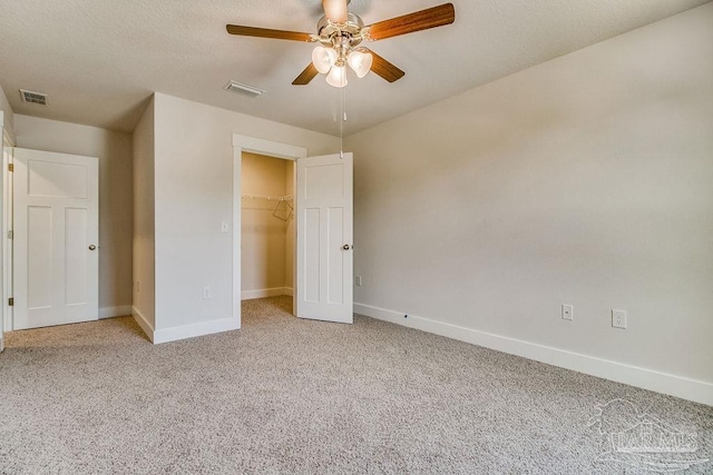 unfurnished bedroom with a walk in closet, a closet, light colored carpet, and ceiling fan