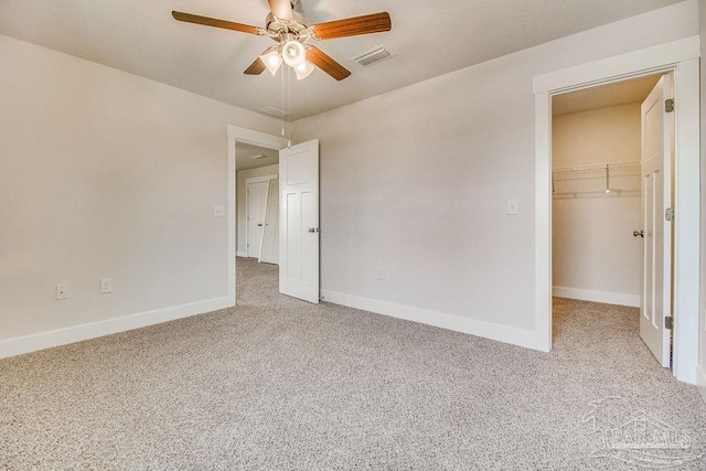 unfurnished bedroom with light carpet, a walk in closet, a closet, and ceiling fan