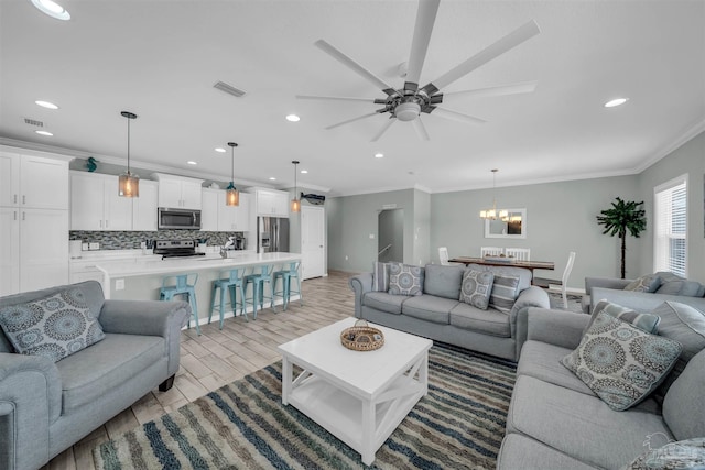 living room featuring light wood-style flooring, visible vents, recessed lighting, ornamental molding, and ceiling fan with notable chandelier