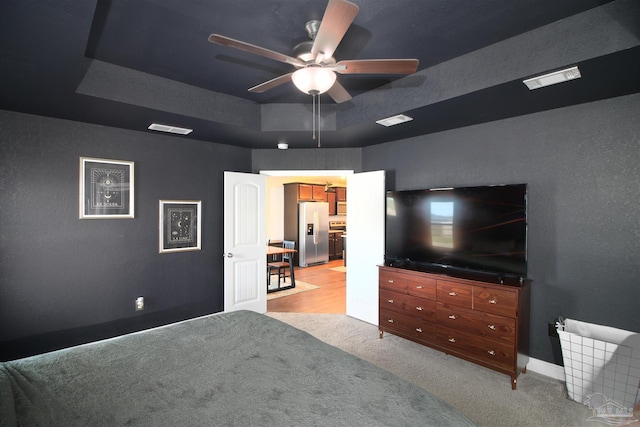 carpeted bedroom with stainless steel fridge, a tray ceiling, and ceiling fan