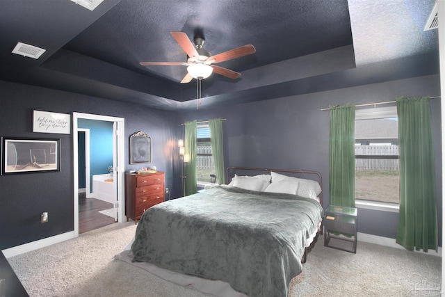 carpeted bedroom featuring ceiling fan, a raised ceiling, and connected bathroom