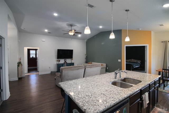 kitchen with ceiling fan, light stone countertops, sink, decorative light fixtures, and a center island with sink