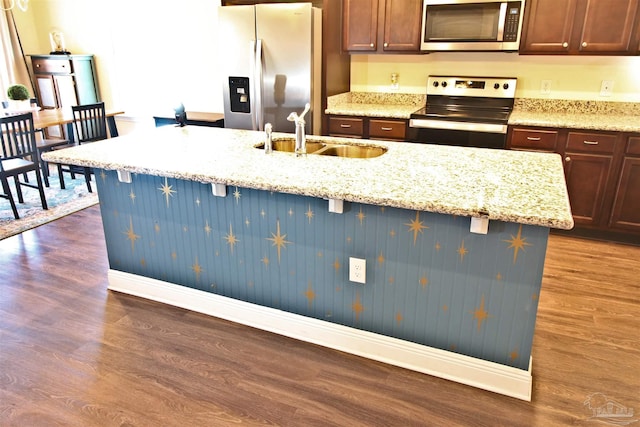 kitchen with light stone countertops, appliances with stainless steel finishes, dark hardwood / wood-style flooring, a kitchen island with sink, and sink