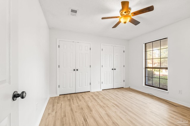 unfurnished bedroom with ceiling fan, light wood-type flooring, a textured ceiling, and multiple closets