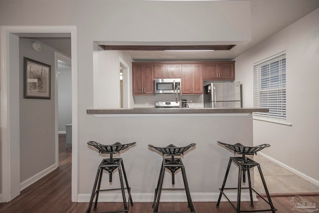 kitchen featuring a kitchen bar, appliances with stainless steel finishes, kitchen peninsula, and dark wood-type flooring