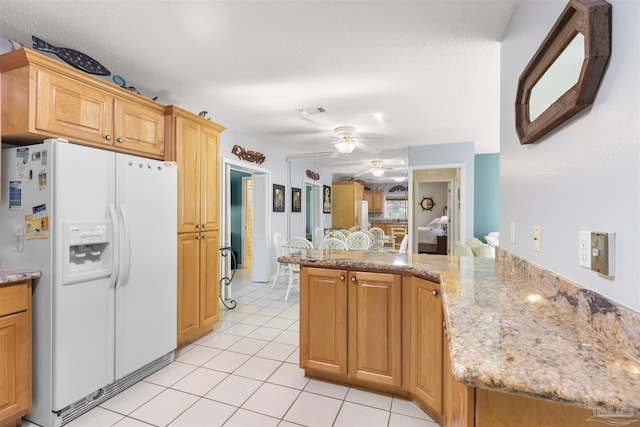 kitchen with light tile patterned floors, kitchen peninsula, ceiling fan, white refrigerator with ice dispenser, and light stone counters