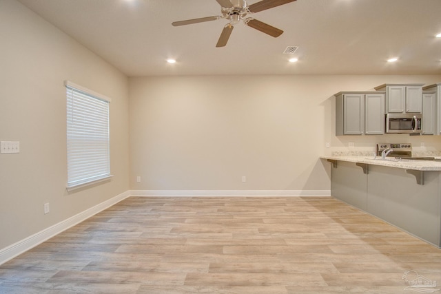 kitchen featuring stainless steel appliances, a kitchen breakfast bar, light hardwood / wood-style flooring, and gray cabinetry