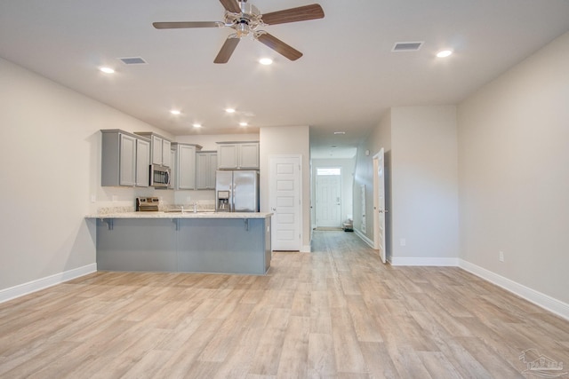 kitchen featuring gray cabinetry, light wood-type flooring, a kitchen breakfast bar, kitchen peninsula, and stainless steel appliances