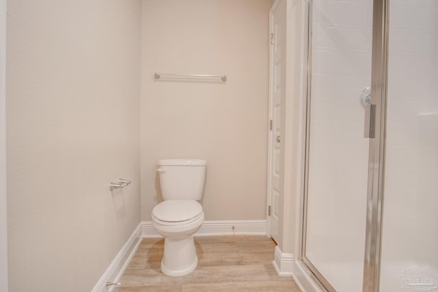 bathroom with hardwood / wood-style floors, a shower with shower door, and toilet