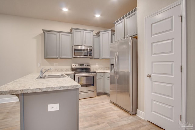 kitchen with gray cabinets, appliances with stainless steel finishes, sink, a kitchen bar, and kitchen peninsula