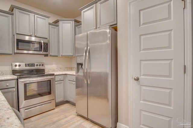 kitchen with appliances with stainless steel finishes, light stone countertops, light hardwood / wood-style floors, and gray cabinetry