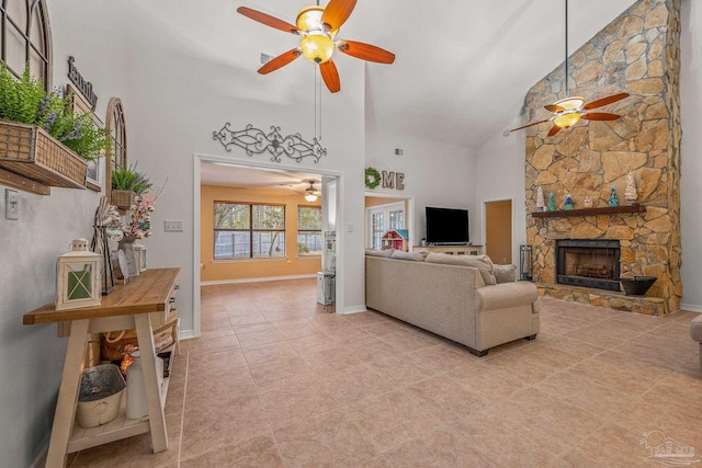 living area featuring light tile patterned floors, baseboards, ceiling fan, a stone fireplace, and high vaulted ceiling