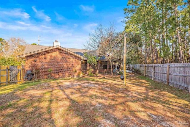 rear view of house featuring a fenced backyard, a chimney, a lawn, and brick siding