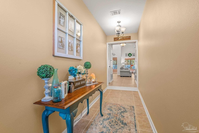 doorway with an inviting chandelier, baseboards, visible vents, and tile patterned floors