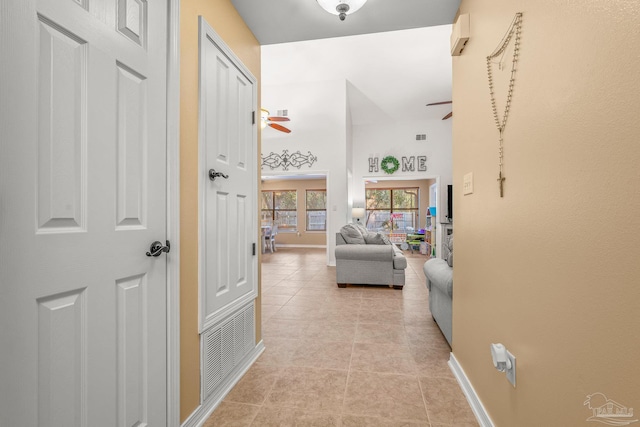 corridor featuring light tile patterned floors, visible vents, a high ceiling, and baseboards