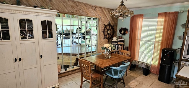 dining area featuring light tile patterned floors, wooden walls, crown molding, and an inviting chandelier