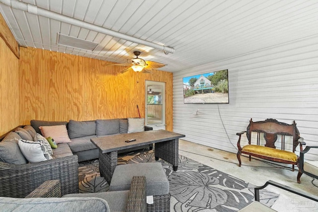 living room with concrete floors, ceiling fan, and wood walls