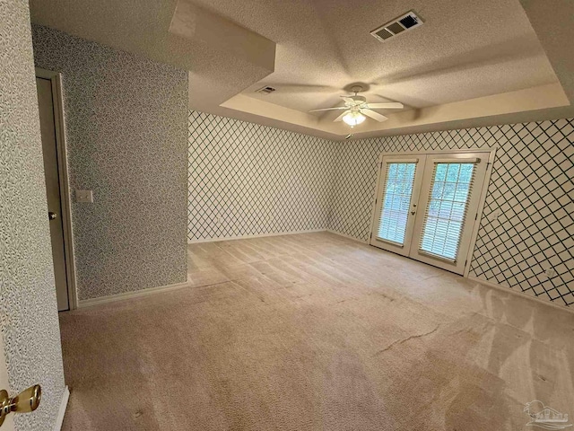 empty room featuring visible vents, carpet flooring, a textured ceiling, and a raised ceiling