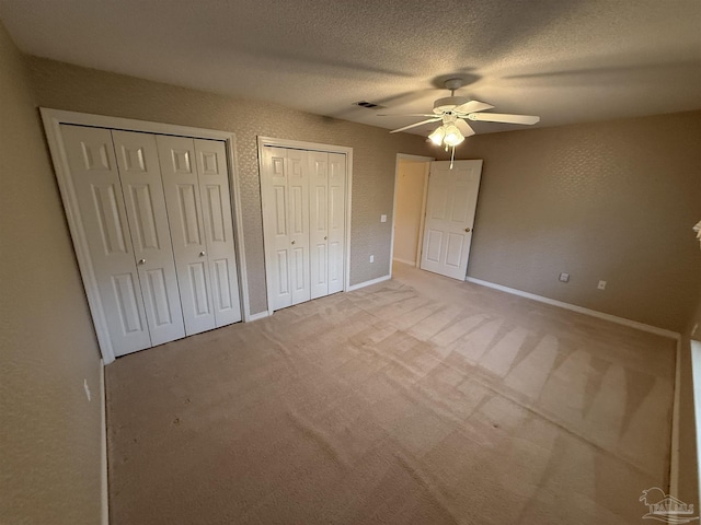 unfurnished bedroom with two closets, a ceiling fan, a textured ceiling, baseboards, and light colored carpet