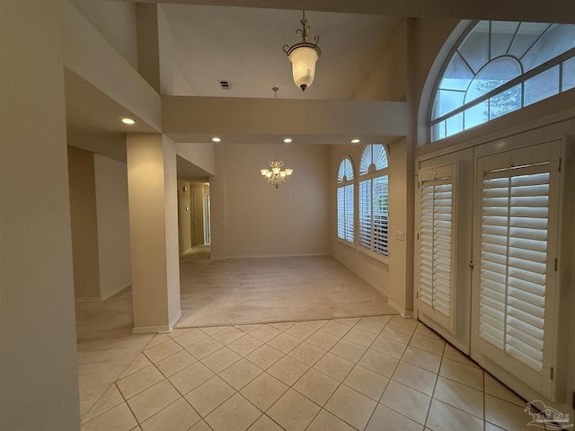 foyer entrance featuring light tile patterned floors, a chandelier, light carpet, and a towering ceiling