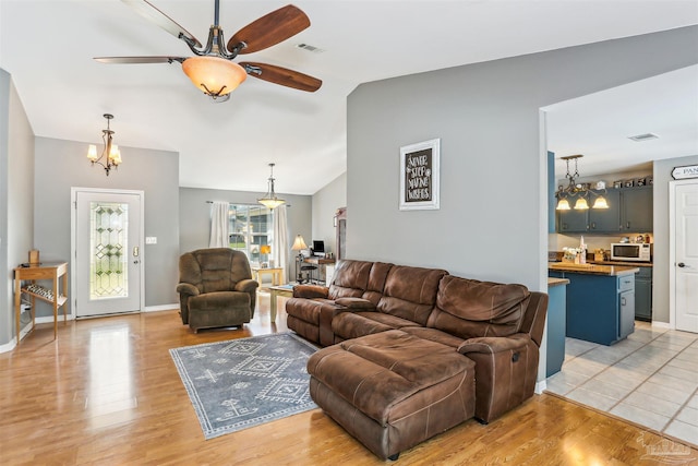 living room featuring lofted ceiling, light wood-type flooring, and ceiling fan with notable chandelier