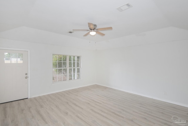 unfurnished room with ceiling fan, lofted ceiling, a tray ceiling, and light wood-type flooring