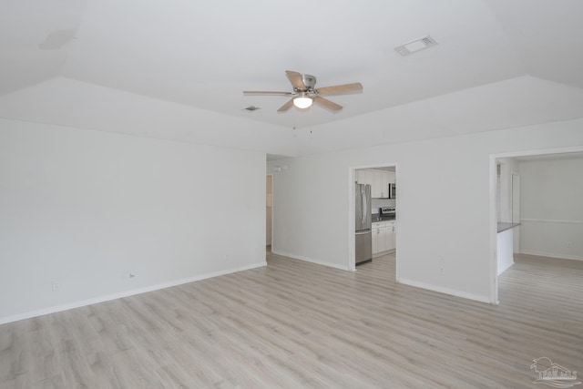 spare room featuring ceiling fan, vaulted ceiling, light wood-type flooring, and a tray ceiling