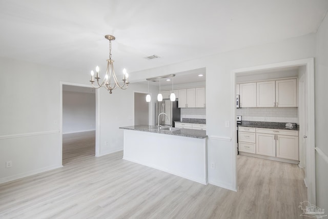 kitchen with sink, tasteful backsplash, decorative light fixtures, light wood-type flooring, and stainless steel refrigerator