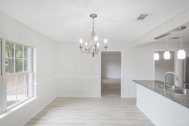 unfurnished dining area featuring a healthy amount of sunlight, sink, a chandelier, and light wood-type flooring