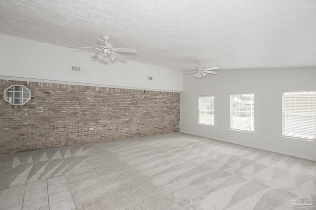 carpeted spare room with ceiling fan, brick wall, and a textured ceiling