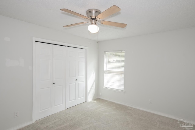 unfurnished bedroom with light carpet, ceiling fan, a closet, and a textured ceiling