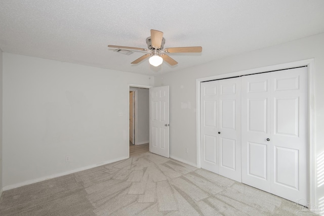 unfurnished bedroom with ceiling fan, light colored carpet, a textured ceiling, and a closet