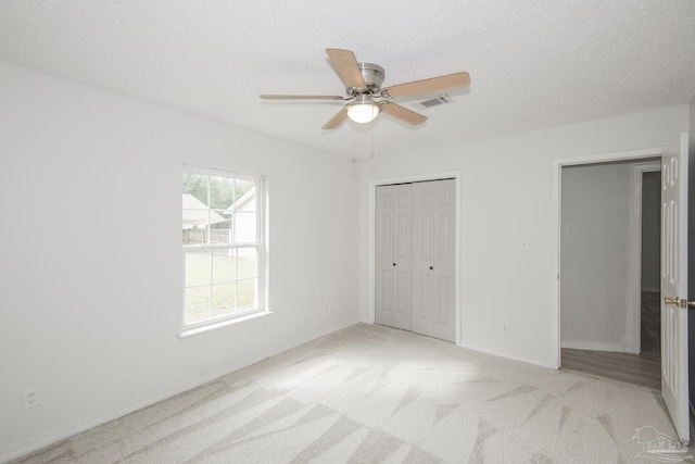 unfurnished bedroom featuring ceiling fan, a closet, light carpet, and a textured ceiling