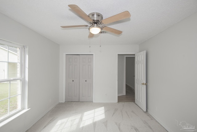 unfurnished bedroom featuring ceiling fan, light colored carpet, a closet, and a textured ceiling