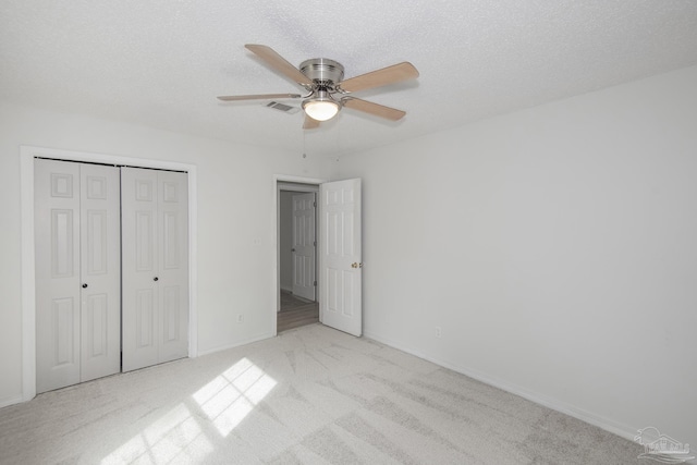 unfurnished bedroom with light carpet, ceiling fan, a closet, and a textured ceiling