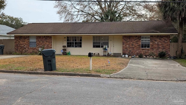 ranch-style house featuring a shingled roof, brick siding, fence, and a front lawn