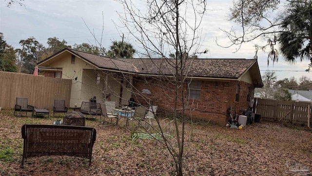 rear view of house with an outdoor fire pit, fence, and brick siding