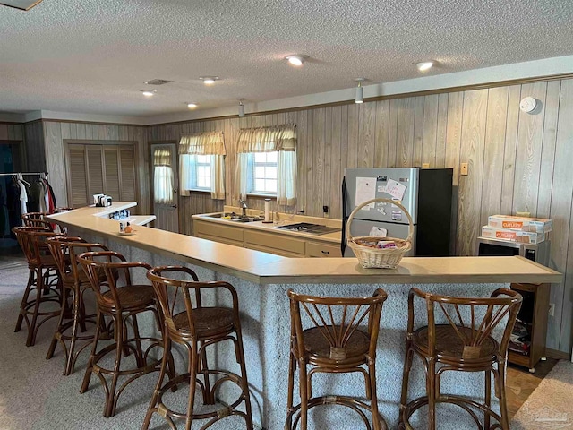 kitchen featuring light carpet, sink, wooden walls, a textured ceiling, and stainless steel refrigerator