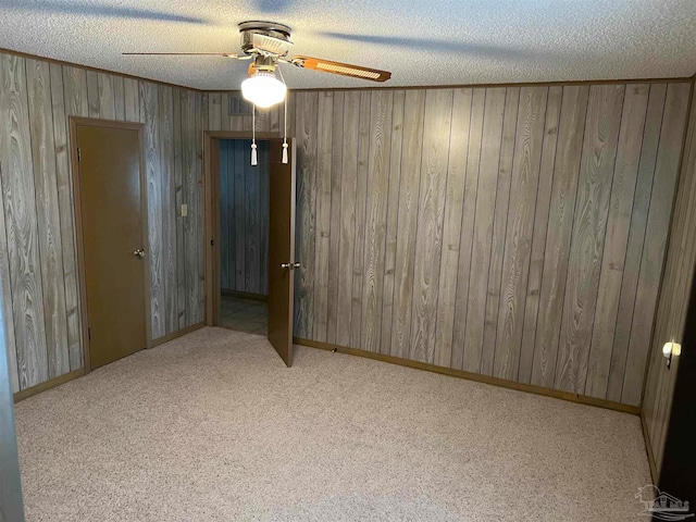 unfurnished bedroom featuring ceiling fan, wooden walls, light carpet, and a textured ceiling