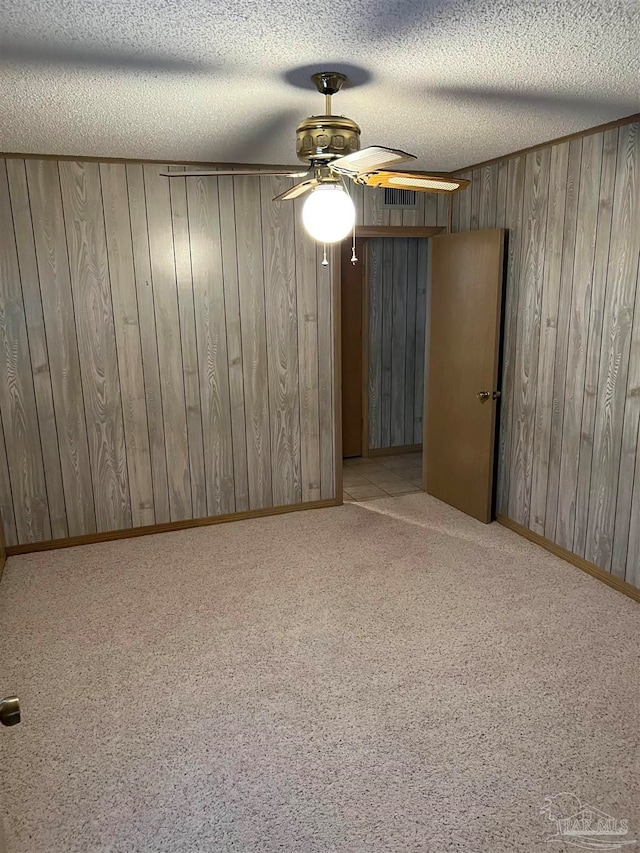 unfurnished room with light carpet, a textured ceiling, and wooden walls