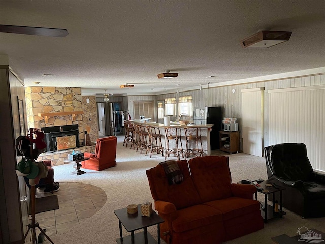 living room featuring carpet flooring, a textured ceiling, a stone fireplace, and ceiling fan