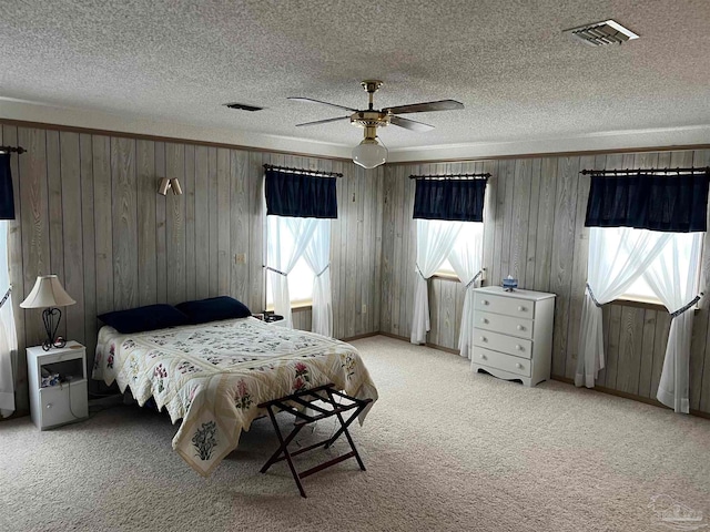 carpeted bedroom featuring ceiling fan, wooden walls, and multiple windows