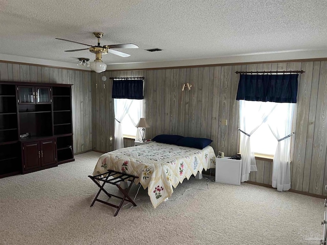 bedroom featuring carpet, ceiling fan, a textured ceiling, and wooden walls