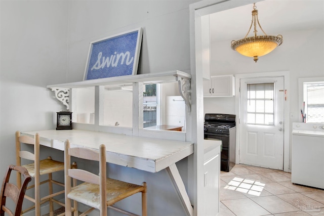 kitchen featuring washer / clothes dryer, hanging light fixtures, black range with gas cooktop, a breakfast bar, and light tile patterned floors