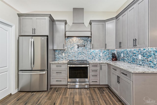 kitchen with custom exhaust hood, gray cabinetry, light stone counters, appliances with stainless steel finishes, and backsplash