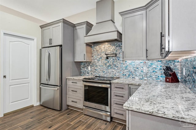 kitchen with light stone counters, gray cabinets, custom range hood, and appliances with stainless steel finishes